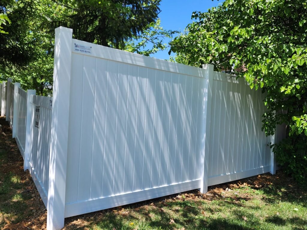 White vinyl fence installed in a landscaped backyard with green grass and trees, showcasing durable outdoor fencing.